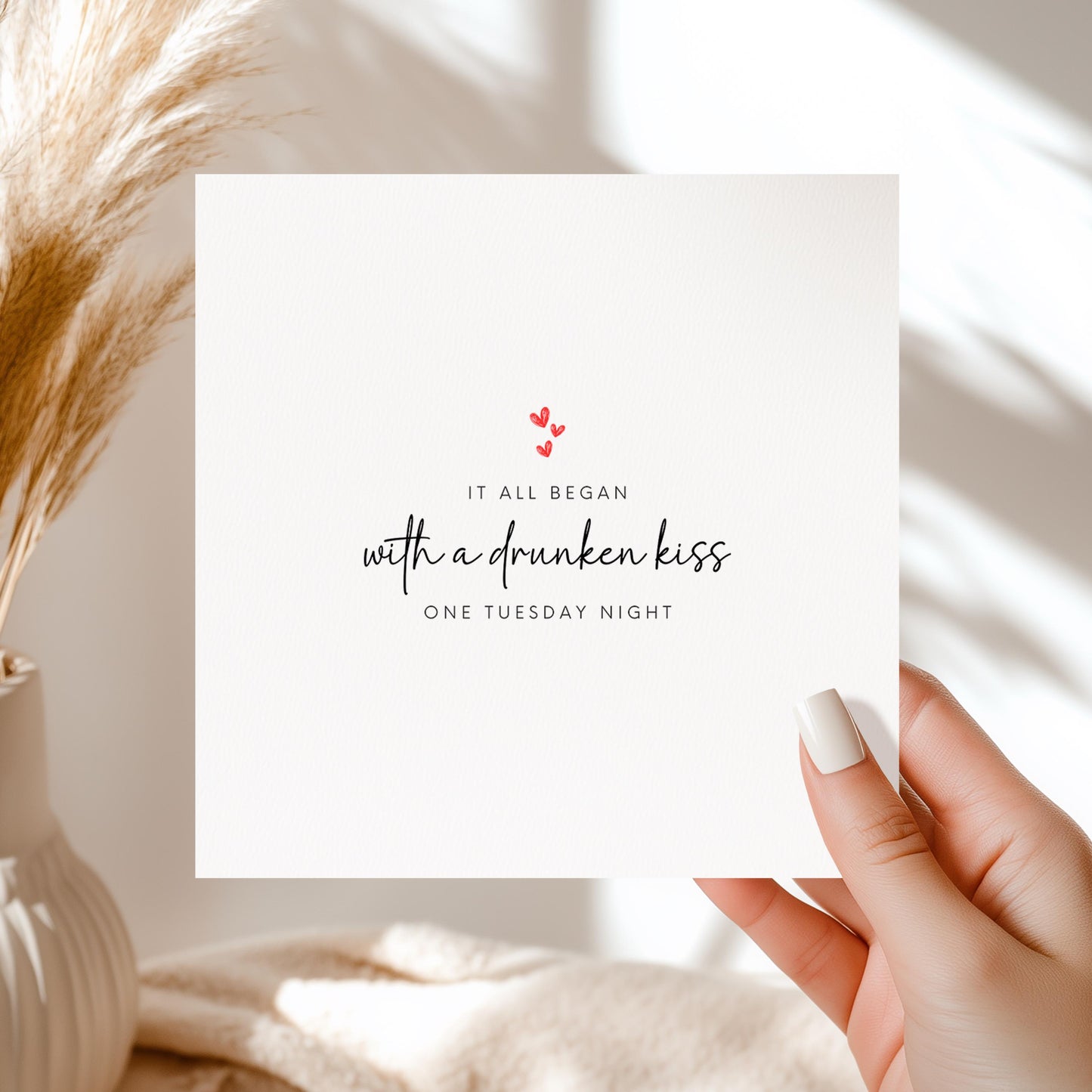 White card with “It all began with a drunken kiss one Tuesday night” design in black script with red hearts.