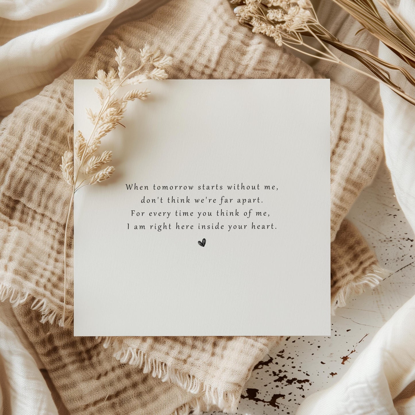 Minimalist sympathy card with heartfelt grief poem printed in black text and a small heart beneath, resting on soft neutral-toned fabric.