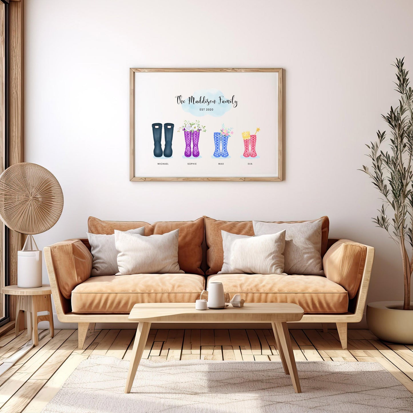 Framed personalised family print featuring four pairs of wellington boots hanging on the wall above a tan sofa with cushions. The room is styled with neutral tones, a coffee table, side table, and decorative plants.