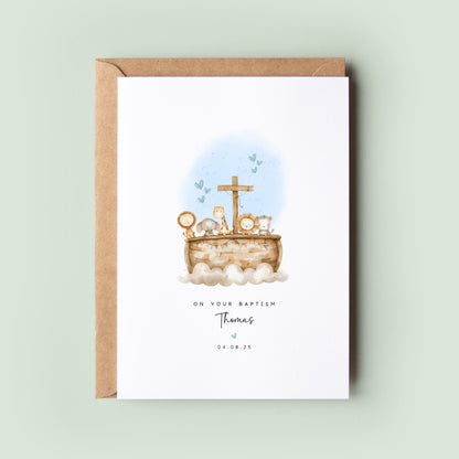 Personalised baptism card featuring a wooden ark with animals, including lions, elephants, and a giraffe, with a cross on top. Soft blue hearts are in the background. Text reads “On your Baptism,” followed by the name and date.