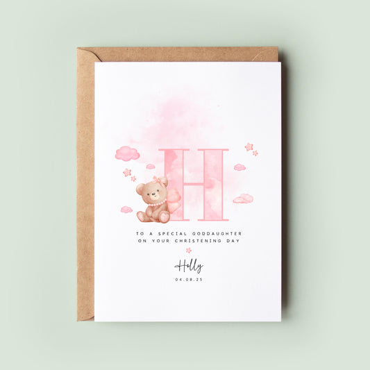 Personalised christening card featuring a large pink letter “H” with a teddy bear holding balloons. The text reads “To a special goddaughter on your christening day,” followed by the name “Holly” and date. Comes with a recycled kraft envelope.