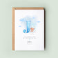 Personalised baptism card featuring a large blue letter “J” with a teddy bear sitting on a cloud. The text reads “To a special son on your baptism day,” followed by the name “Joshua” and date. Comes with a recycled kraft envelope.