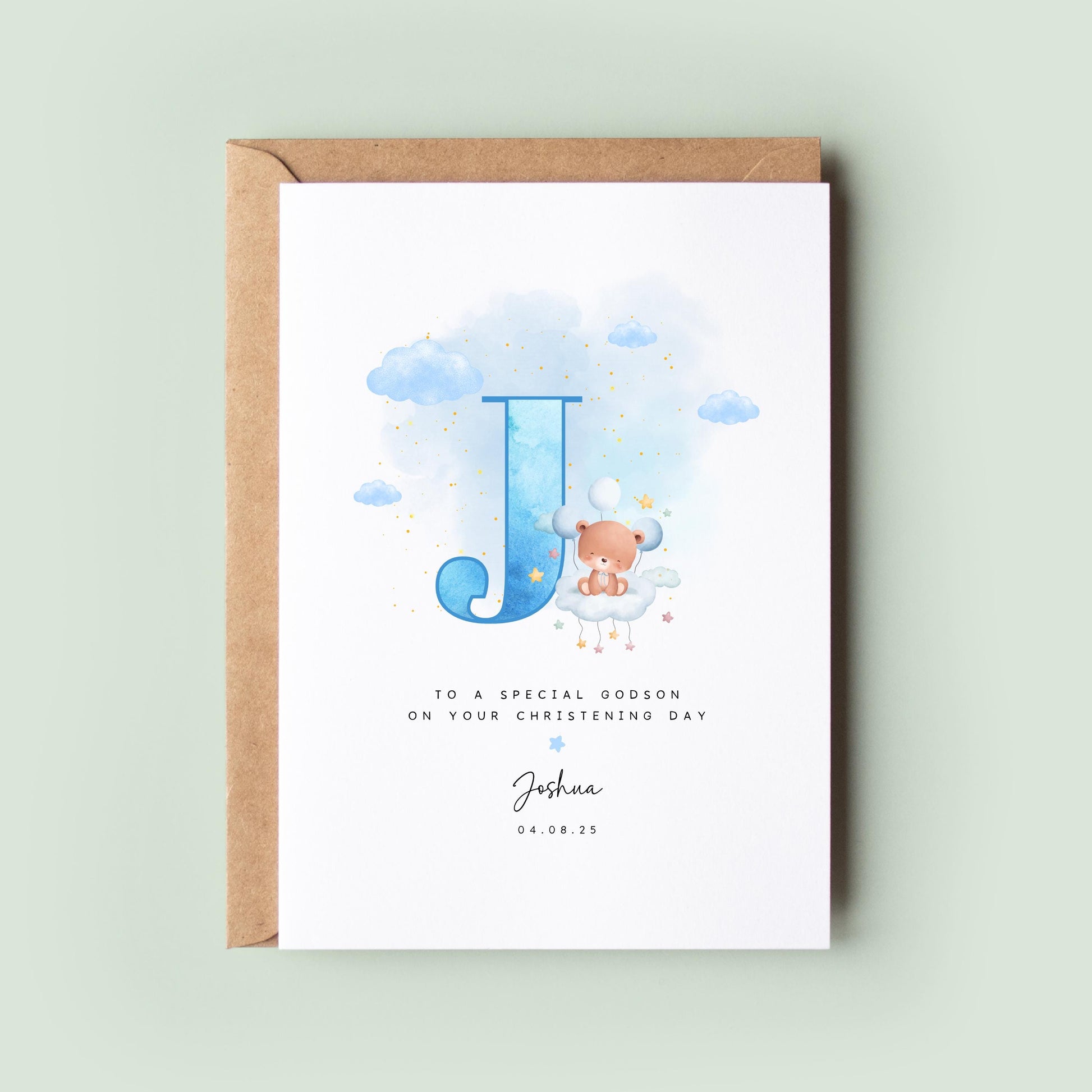 Personalised christening card featuring a large blue letter “J” with a teddy bear sitting on a cloud. The text reads “To a special godson on your christening day,” followed by the name “Joshua” and date. Comes with a recycled kraft envelope.