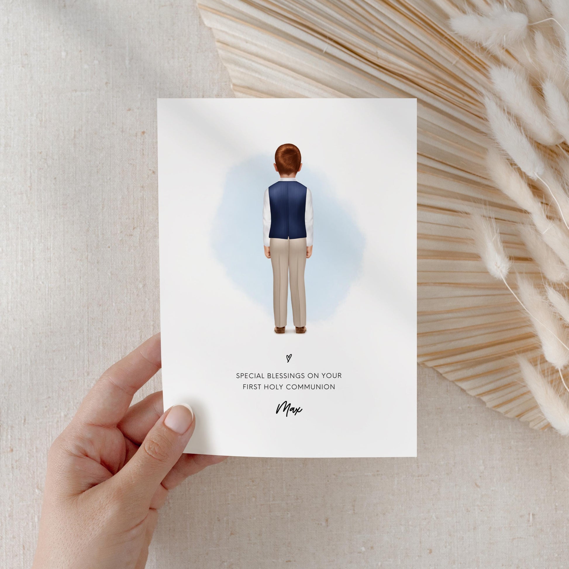 Hand holding a Holy Communion card featuring a boy with brown hair facing away, dressed in a navy blue waistcoat, white shirt, and beige trousers. The design includes the message, “Special blessings on your First Holy Communion,” with a name beneath.