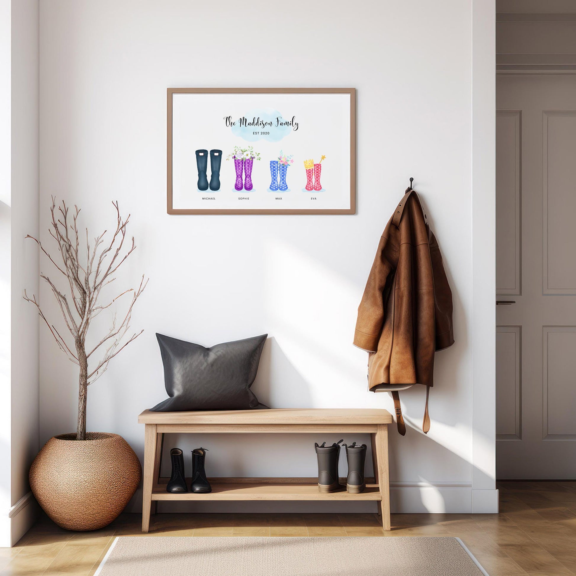 Framed personalised family print featuring four pairs of wellington boots hanging on a wall in a modern, minimalist hallway. A bench, coat, and boots are arranged below the print, with a decorative plant on the side.